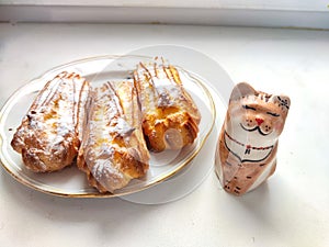 Delectable Dessert Pastries With Charming Porcelain Cat Figurines. Piped cakes sprinkled with sugar beside whimsical cat