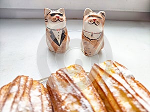 Delectable Dessert Pastries With Charming Porcelain Cat Figurines. Piped cakes sprinkled with sugar beside whimsical cat photo