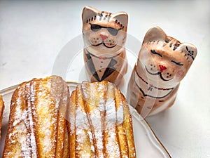 Delectable Dessert Pastries With Charming Porcelain Cat Figurines. Piped cakes sprinkled with sugar beside whimsical cat photo