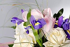 Delicate beautiful bouquet of iris, roses and other flowers on gray background