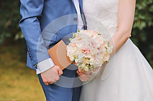Delicate beautiful wedding bouquet of pink peony roses and orchids in the hands of the bride, in the hands of the groom brown book