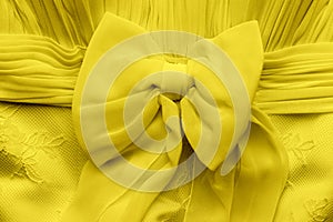 Delicate bright yellow illuminating bow on a wedding dress closeup. Textile fabric decoration background