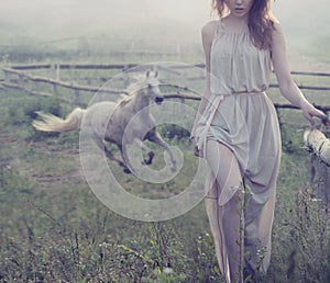 Delicate brunette posing with horse in the background