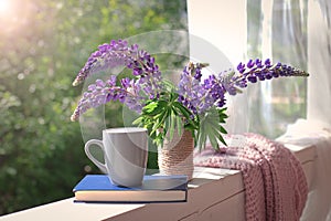 Delicate composition with purple lupines bouquet, cup and book