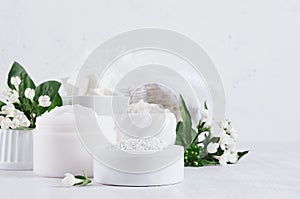 Delicate elegance light cosmetics products for body and skin care with fresh white flowers and green leaves on white wood board.