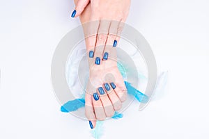 Delicate female hands with perfect manicure blue on a gray background with decorative feathers. Concept of self-care