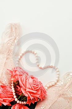 Delicate feminine theme. Pink coral roses trend color on a pale pink bra and pearl necklace on a white background. top view. close