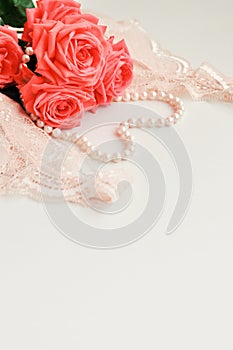 Delicate feminine theme. Pink coral roses trend color on a pale pink bra and pearl necklace on a white background. top view. close