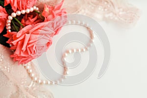 Delicate feminine theme. Pink coral roses trend color on a pale pink bra and pearl necklace on a white background. top view. close