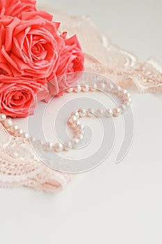 Delicate feminine theme. Pink coral roses trend color on a pale pink bra and pearl necklace on a white background. top view. close