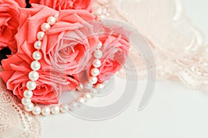 Delicate feminine theme. Pink coral roses trend color on a pale pink bra and pearl necklace on a white background. top view. close