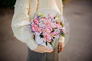 Delicate flower arrangement in square box in woman`s hand.