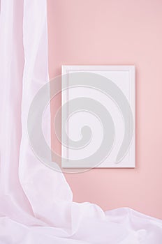 Delicate home decor with blank rectangle photo frame hanging on pastel pink wall, flow of silk curtain, vertical. Mock up.