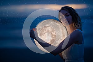 Delicate image of an angel, a girl with the moon in her hands on the night beach. artistic photography. Fairy tale and riddle.