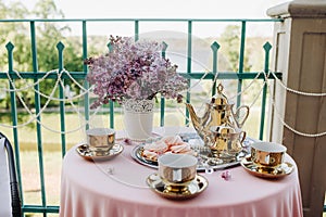 Delicate morning tea table setting with lilac flowers, antique spoons and dishes on a table with a pink tablecloth