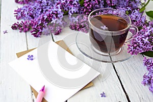 Delicate morning tea table setting with lilac flowers, a transparent cup of tea and a saucer and a white vase, white and