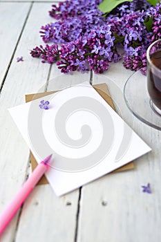 Delicate morning tea table setting with lilac flowers, a transparent cup of tea and a saucer and a white vase, white and