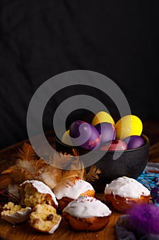 Delicate muffins in white glaze and unusually painted eggs in a ceramic cup with paraphernalia of decorative feathers.