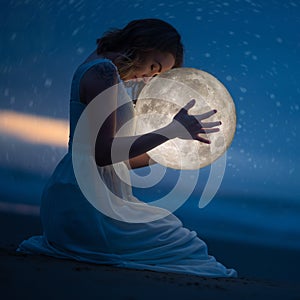 Delicate photography, Astrology, Women`s magic. Beautiful attractive girl on a night beach with sand and stars hugs the moon, art