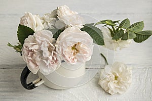 Delicate pink roses are in the old cup.