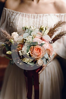 Delicate, stylish bouquet of roses, peonies in the hands of the bride in a wedding dress. Vertical beautiful wedding concept