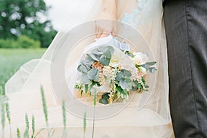 Delicate wedding bouquet in the hands of the bride on the background of the wedding dress