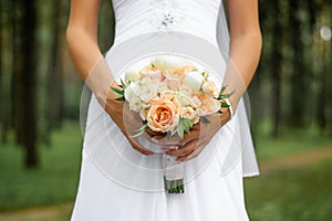 Delicate wedding bouquet of peach roses and white peonies in the bride`s hand