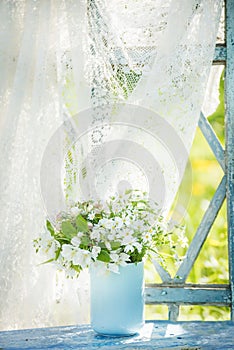 Delicate white forest flowers in a blue cup on an old window overlooking the sunny garden. Retro vintage style.