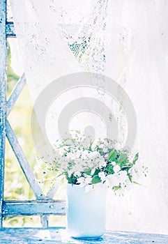 Delicate white forest flowers in a blue cup on an old window overlooking the sunny garden. Retro vintage style.