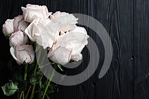 Delicate white roses on black wooden background close up, beautiful light pink flowers bouquet on dark gray wood, greeting card
