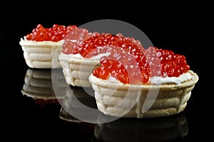 Red caviar in tartlet, isolated over black photo