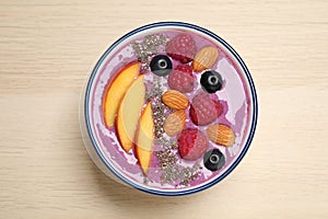 Delicious acai smoothie with fruits and almonds in bowl on wooden table, top view