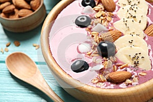 Delicious acai smoothie with granola and almonds in dessert bowl on light blue wooden table, closeup