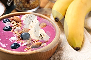Delicious acai smoothie with granola and almonds in dessert bowl on table, closeup