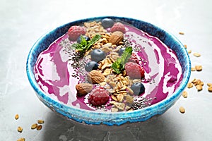 Delicious acai smoothie with granola and berries in bowl on light marble table