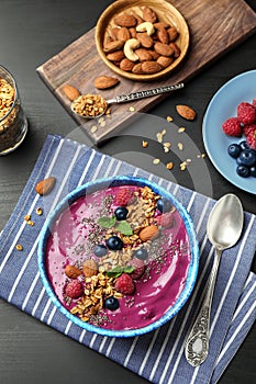 Delicious acai smoothie with granola and berries in bowl served on dark wooden table, flat lay