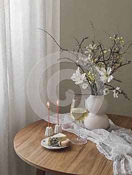 Delicious aperitif - blue cheese, glass of white wine, candles, flowers in a vase on a wooden table