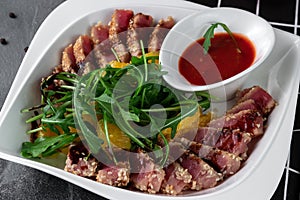 Delicious appetizer with sliced bacon, arugula, orange and red sauce on grey table. Traditional dish menu served in a restaurant,