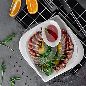 Delicious appetizer with sliced bacon, arugula, orange and red sauce on grey table. Traditional dish menu served in a restaurant,