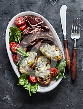 Delicious appetizer, tapas, lunch plate - beef steak, vegetables salad and baked potatoes with blue cheese on a dark background,