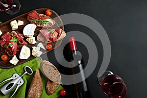 Delicious appetizer to wine - ham, cheese, baguette slices, tomatoes, served on a wooden board, and glass with red wine