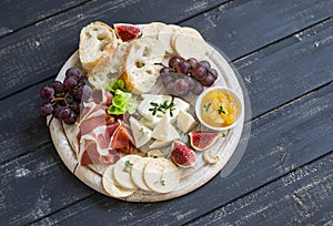 Delicious appetizer to wine - ham, cheese, grapes, crackers, figs, nuts, jam, served on a light wooden board