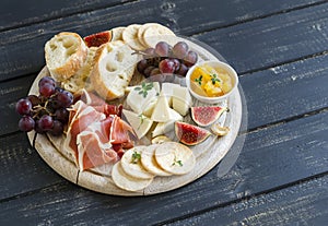 Delicious appetizer to wine - ham, cheese, grapes, crackers, figs, nuts, jam, served on a light wooden board