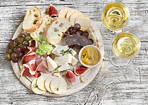 Delicious appetizer to wine - ham, cheese, grapes, crackers, figs, nuts, jam, served on a light wooden board, and two glasses with