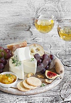 Delicious appetizer to wine - ham, cheese, grapes, crackers, figs, nuts, jam, served on a light wooden board, and two glasses with