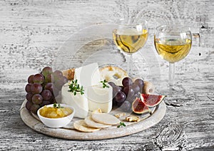 Delicious appetizer to wine - ham, cheese, grapes, crackers, figs, nuts, jam, served on a light wooden board, and two glasses with