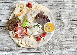 Delicious appetizer to wine - ham, cheese, grapes, crackers, figs, nuts, jam, served on a wooden board