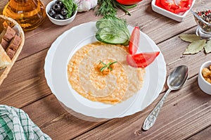 Delicious appetizing pea porridge garnish with fresh vegetables on a white plate on a wooden background