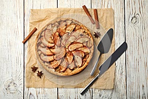 Delicious apple pie, cinnamon, spatula and knife on white wooden table, flat lay