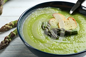 Delicious asparagus soup in bowl on white table, closeup